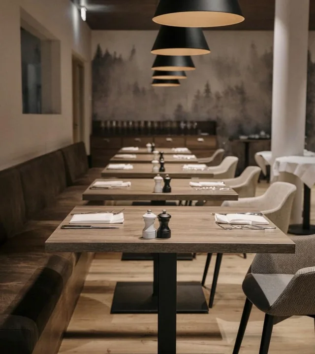 Restaurantansicht mit Holztischen, heller Polsterung, Wandgestaltung und dunklen Pendelleuchten