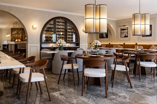Restaurantgastraum mit runden Tischen, Weinregal und großformatigen Pendelleuchten